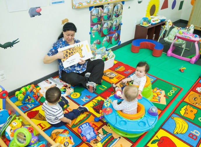 Adult reading a book to three children in a play area