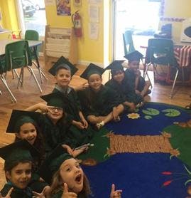 Children in graduation caps and gowns sitting on a rug