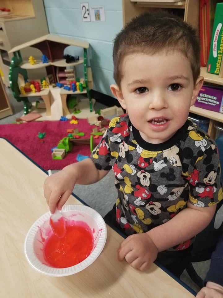 Child stirring red liquid in a bowl at a table