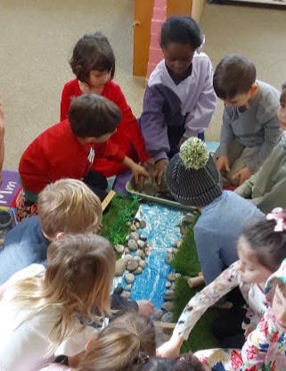 Children gathered around a miniature landscape with a river
