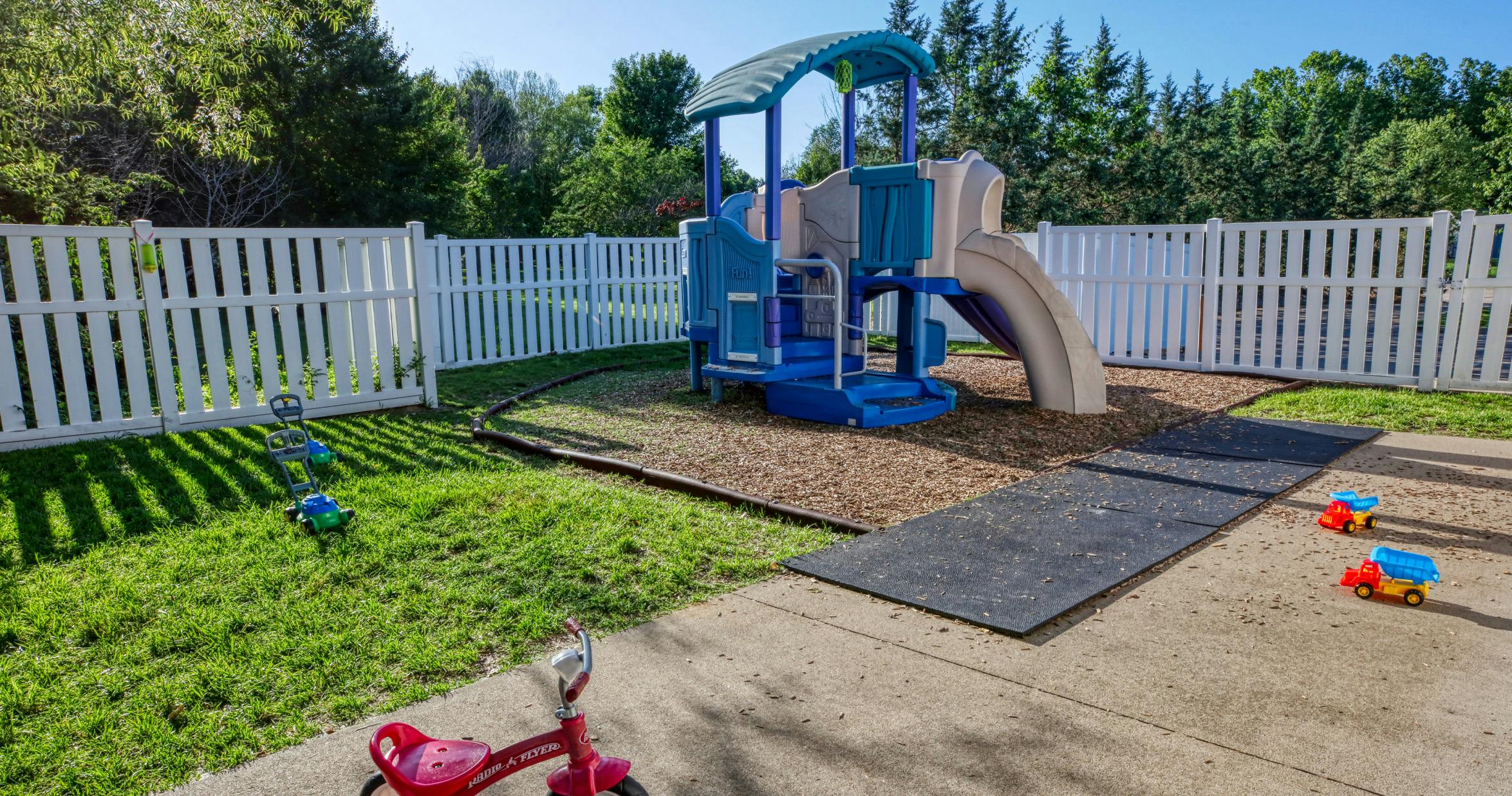 A children's playground with a slide structure, tricycle, toy lawnmower, and trucks