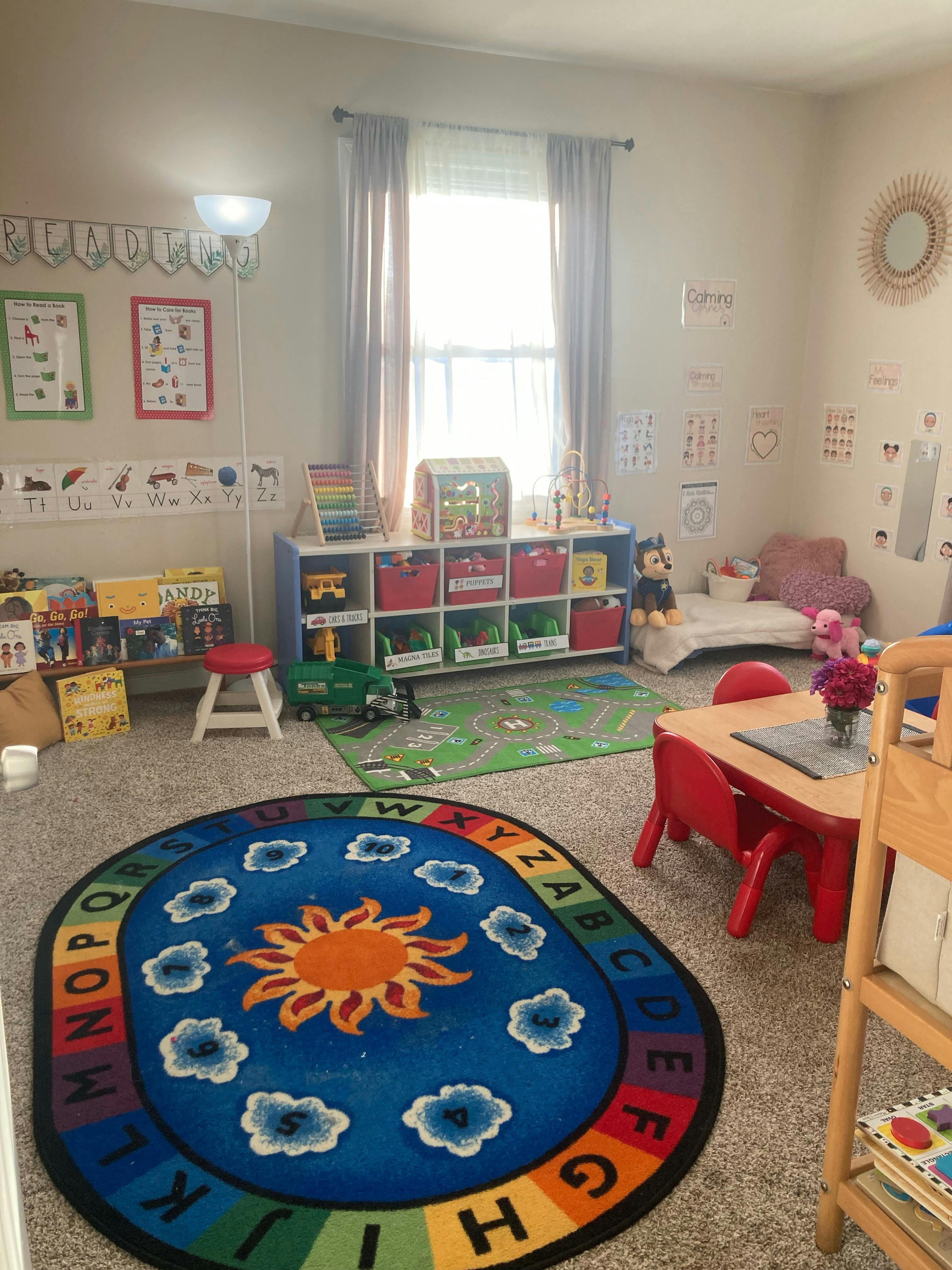 A colorful playroom with a sun and alphabet rug, toys, and small furniture