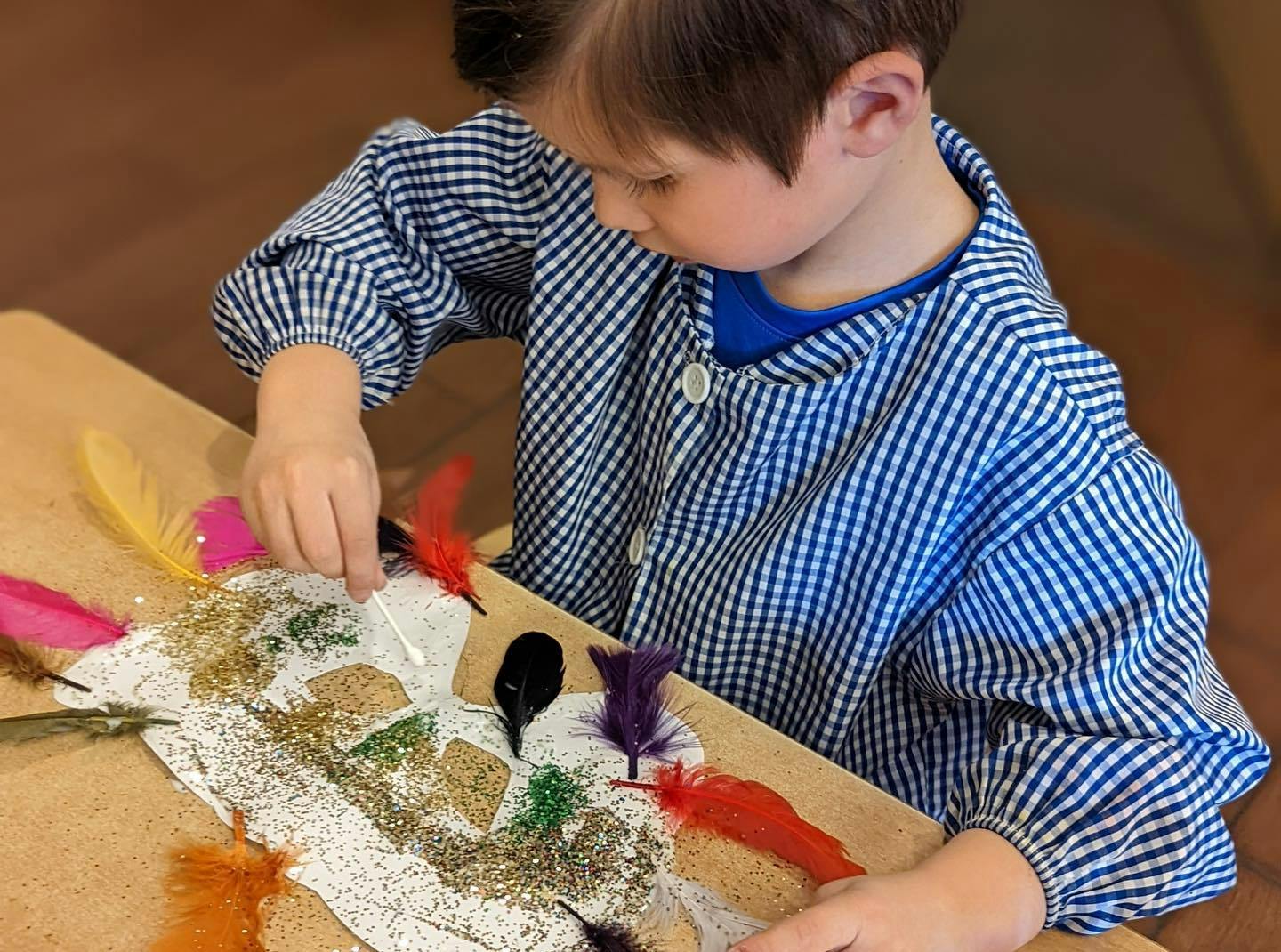 Child decorating a craft with feathers and glitter
