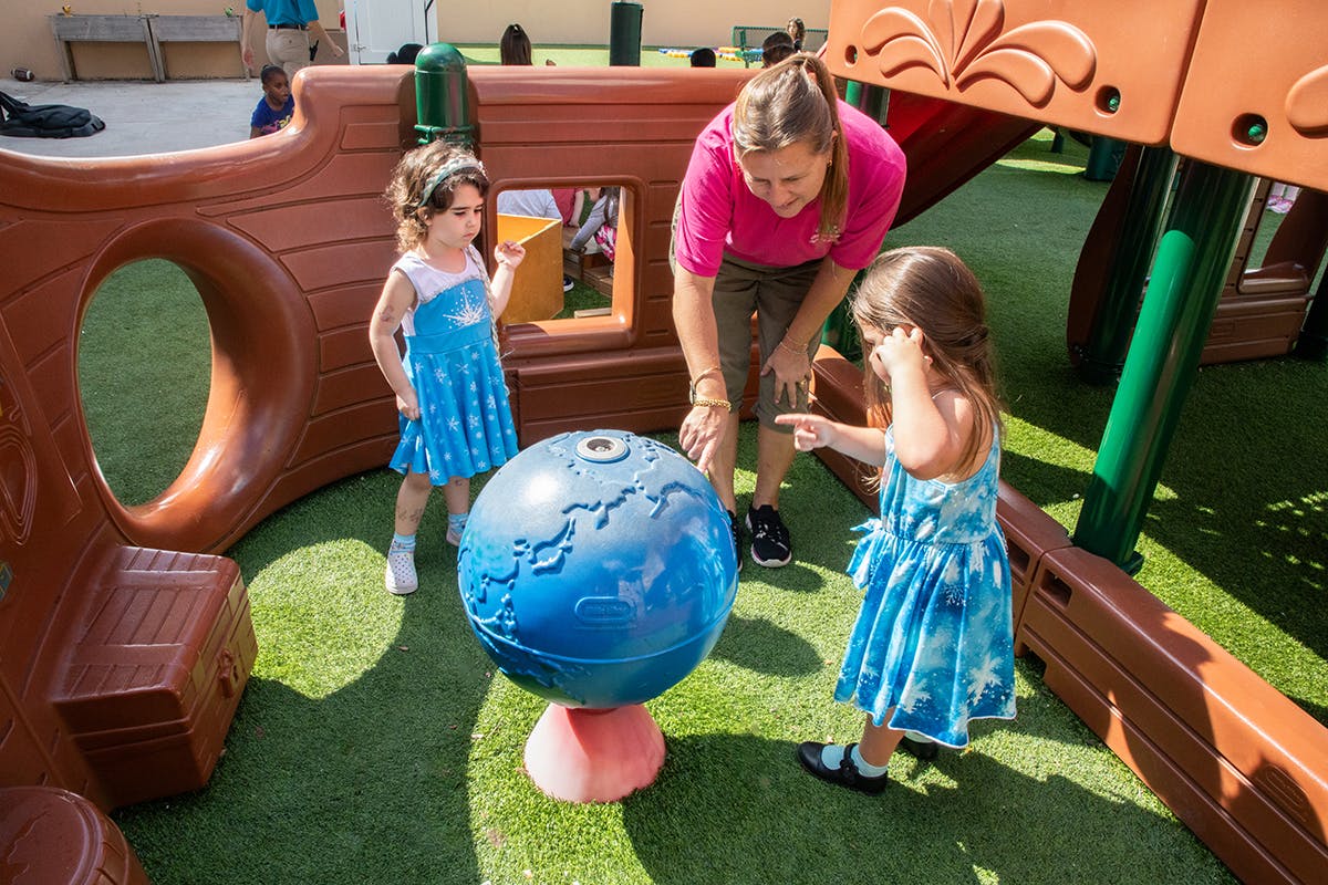 Adult and two children interacting with a globe on a playground