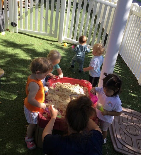 Children playing in a sandbox with an adult nearby