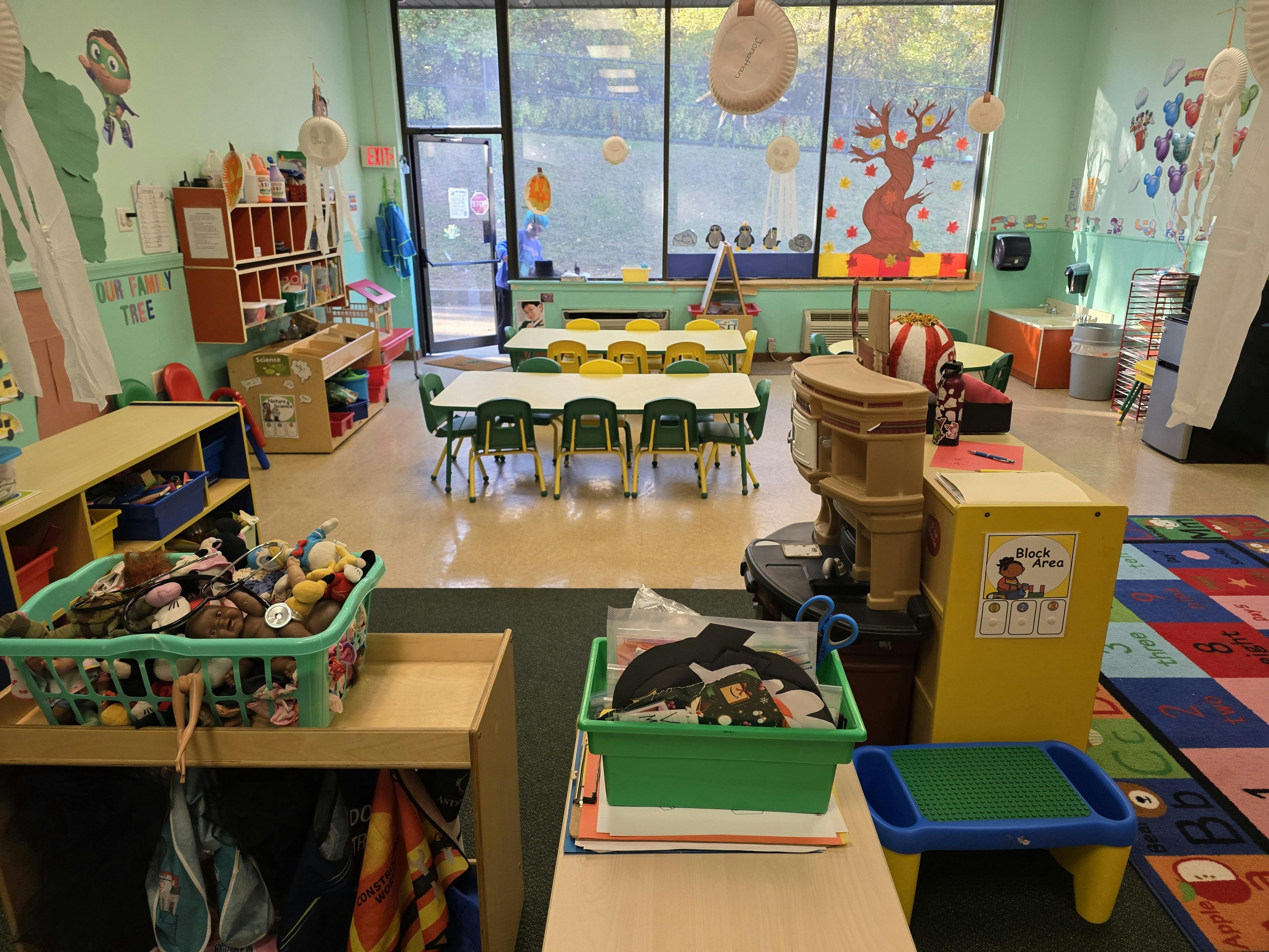 Classroom with tables and chairs, toys in bins, and decorations on the walls
