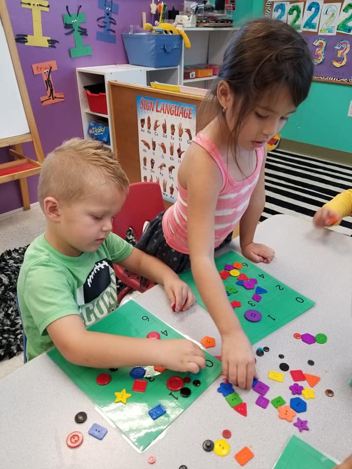 Two children playing with colorful shapes and buttons at a table