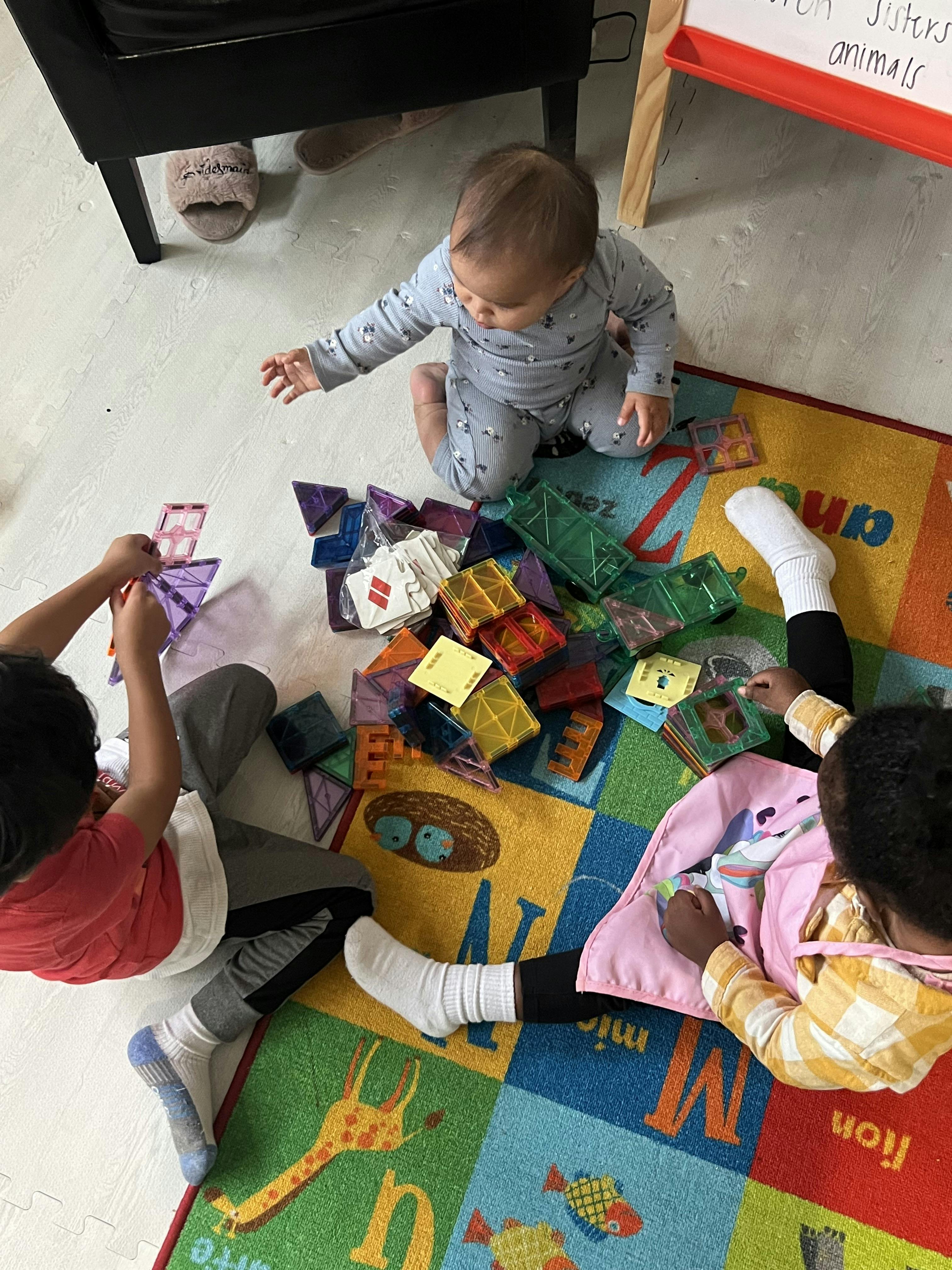 Three children playing with magnetic building tiles on a colorful rug