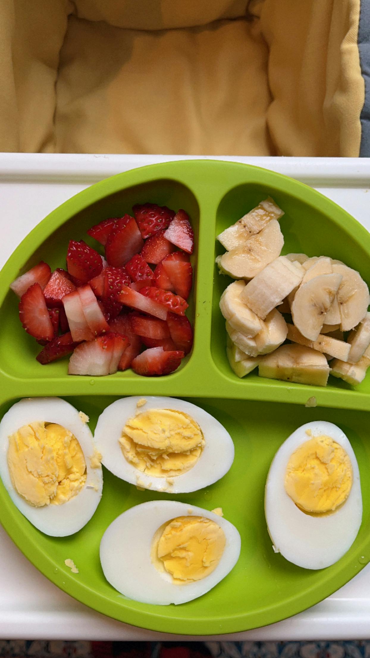 Green plate with sliced strawberries, bananas, and hard-boiled eggs
