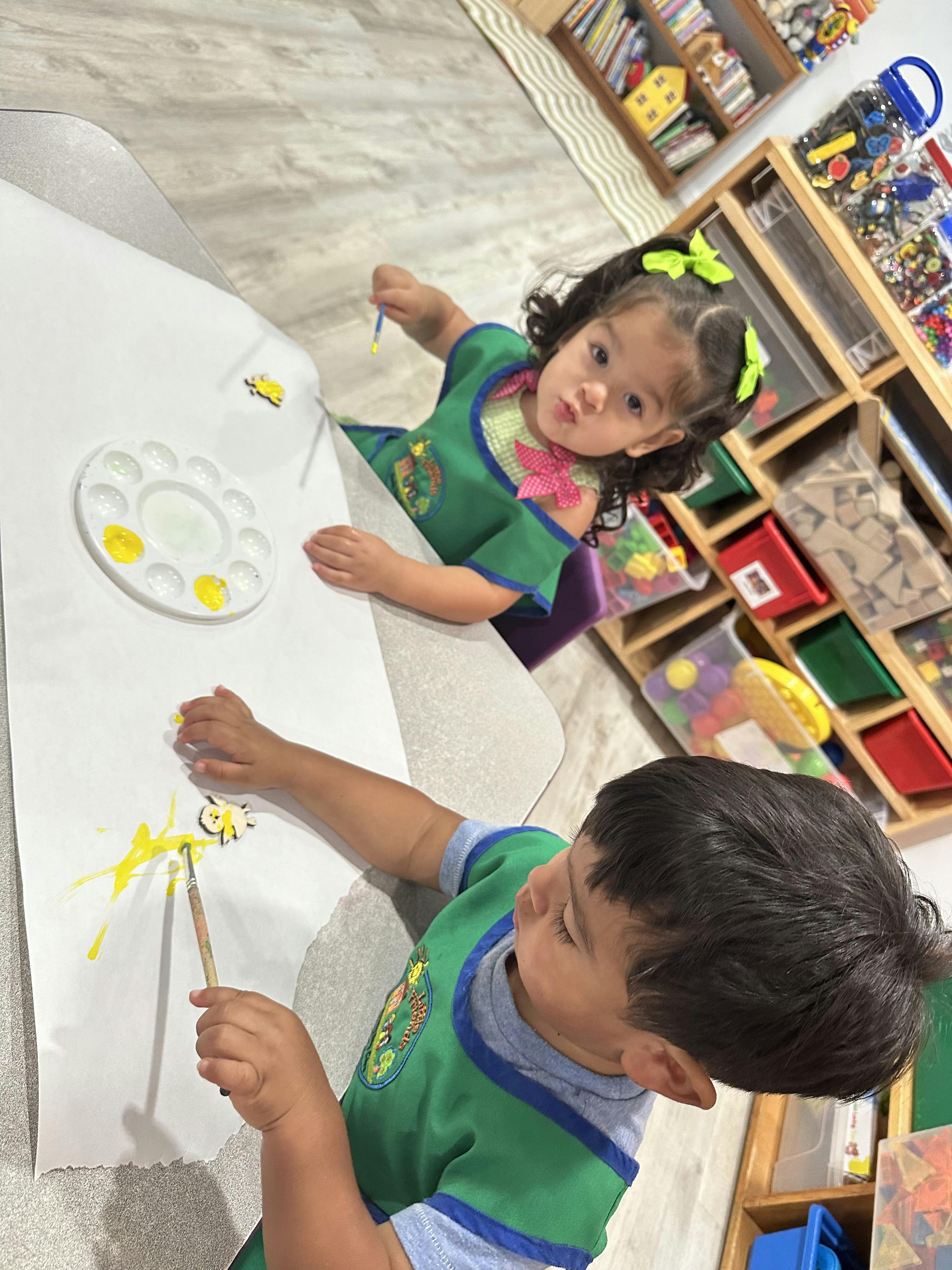 Two children painting on paper with yellow paint