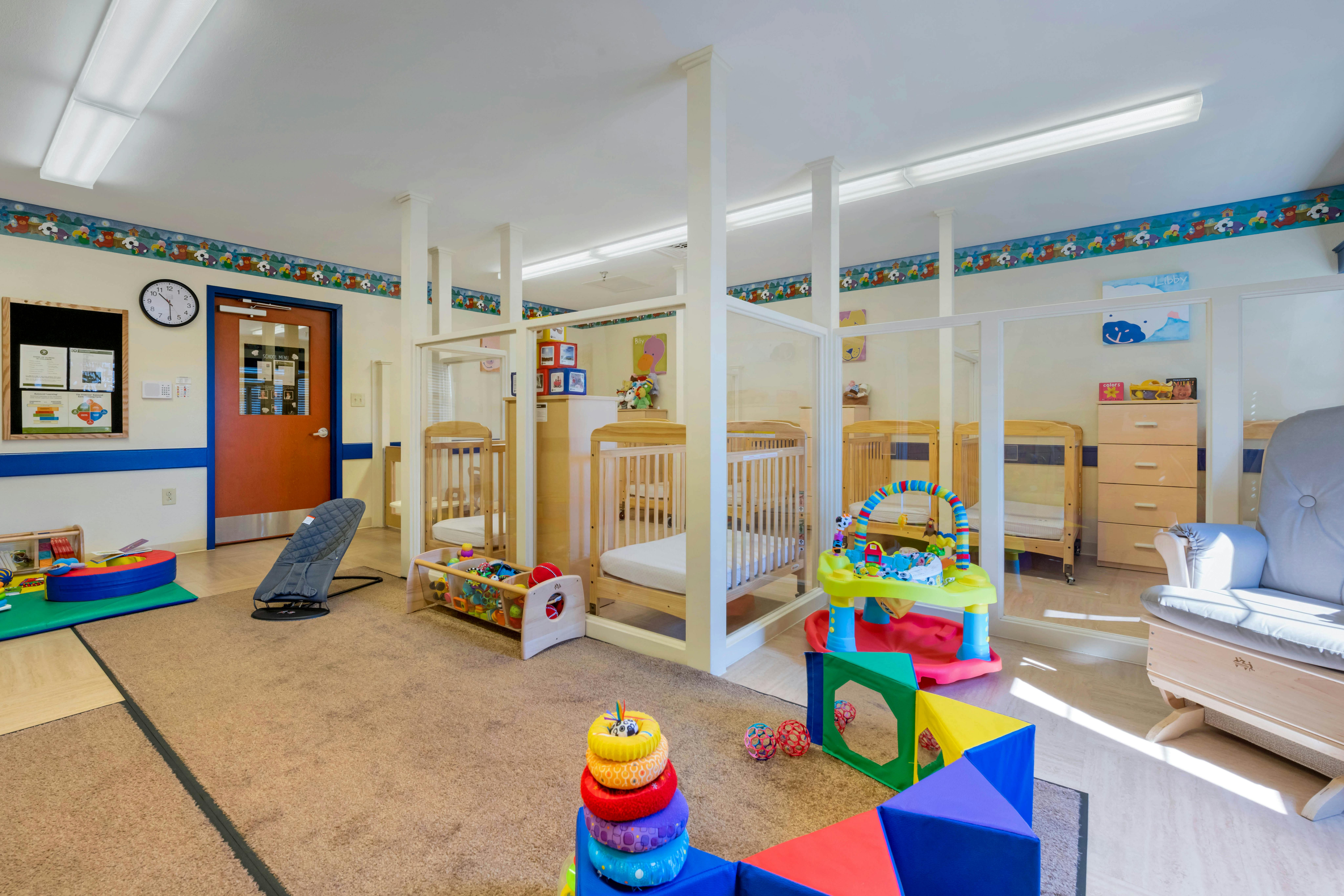 A childcare room with multiple cribs, play mats, toys, and a rocking chair