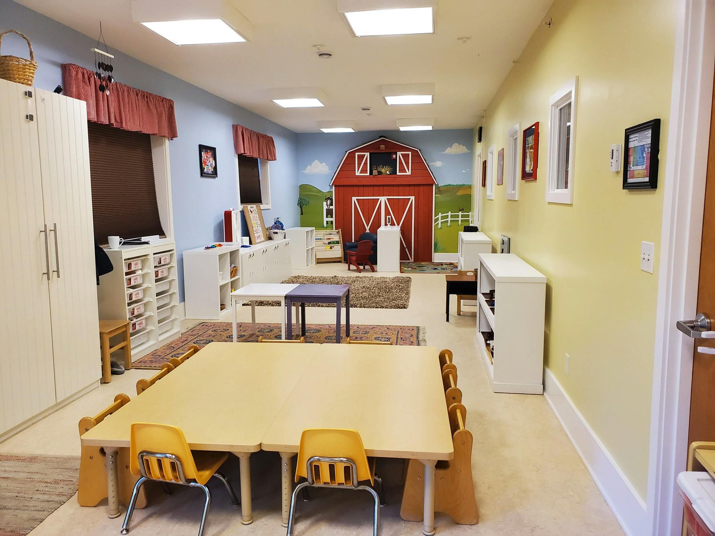 An empty children's classroom with small tables, chairs, and a barn mural