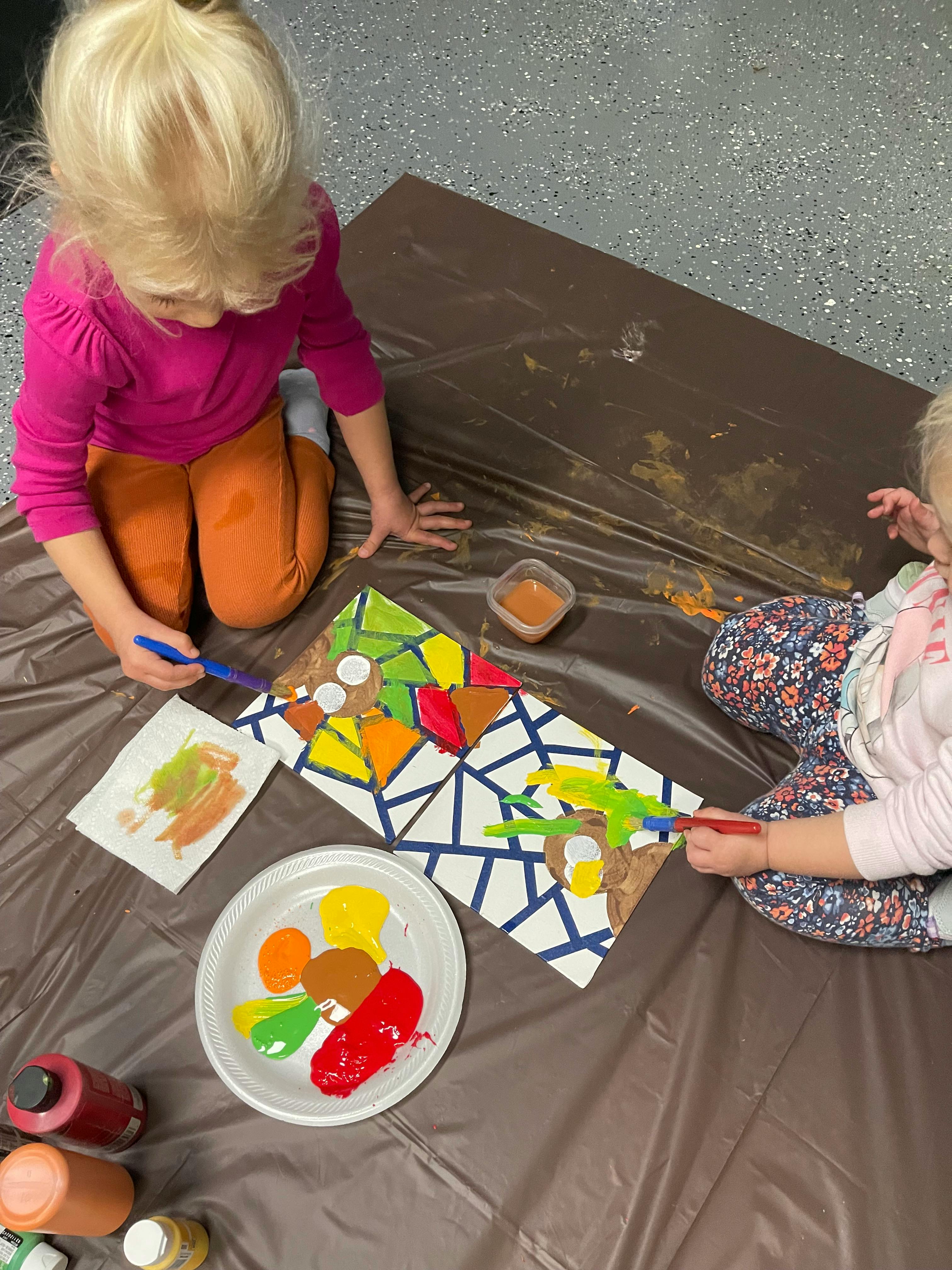 Two children painting on a brown tarp