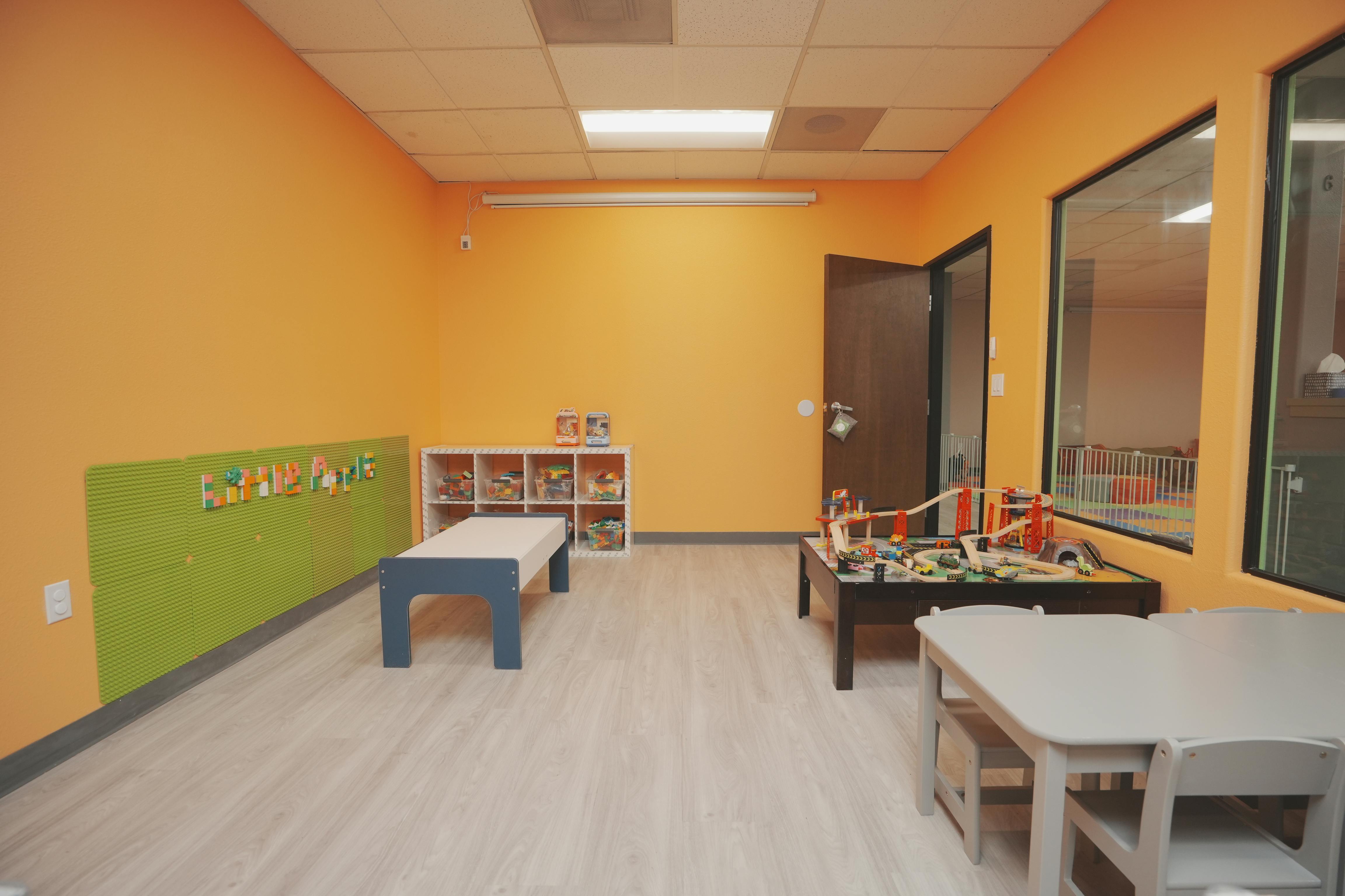 Empty classroom with orange walls, green wainscoting, and small tables