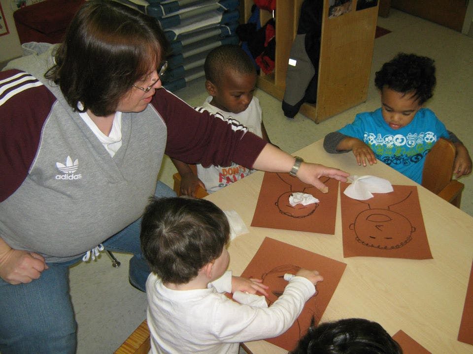 Person helping three children with craft projects at a table