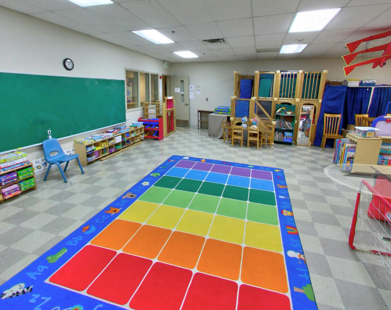 Classroom with a rainbow-colored rug, chalkboard, and small tables and chairs