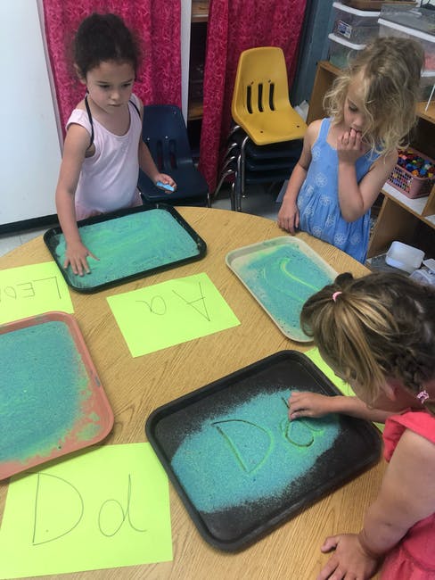 Children learning to write letters using sand trays in a classroom