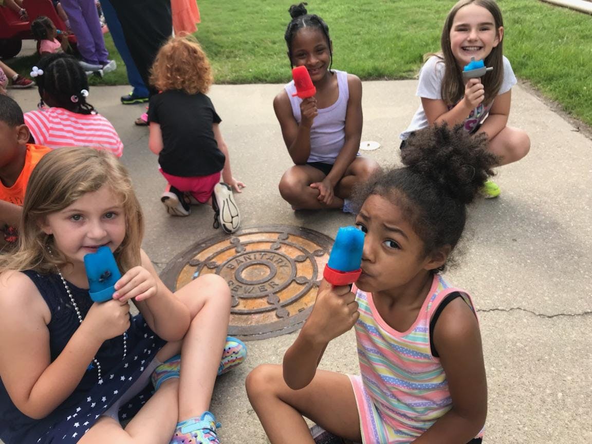 Children sitting on pavement eating popsicles