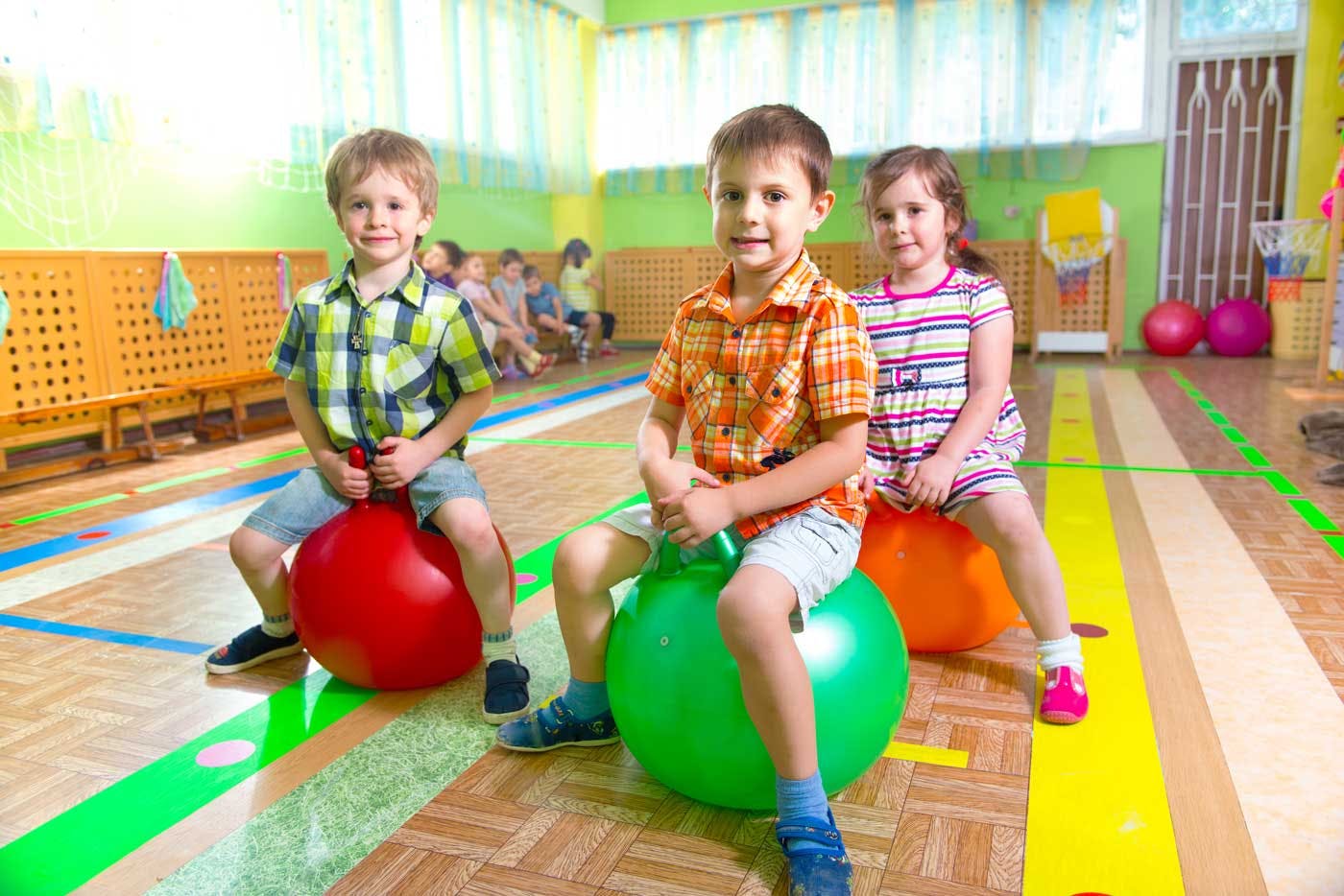 Three children sitting on bouncy balls in a classroom