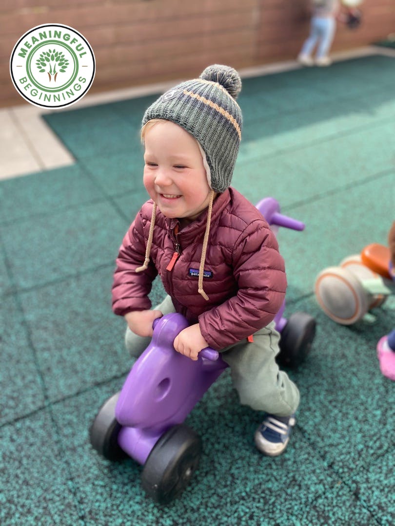 Child in a knit hat on a purple ride-on toy on a playground