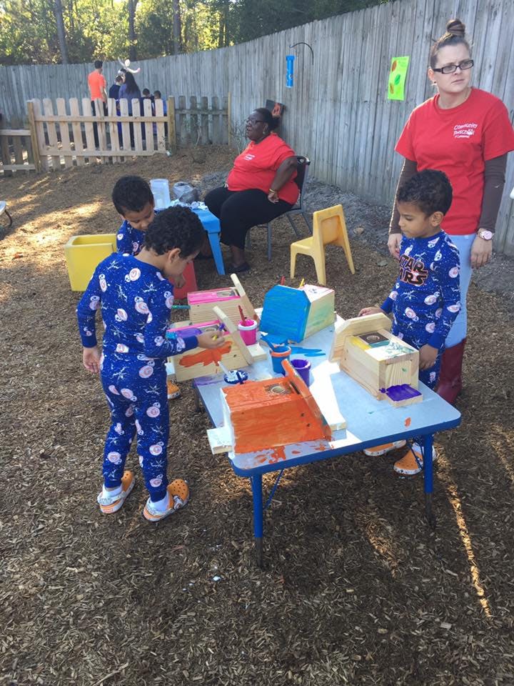 Children painting wooden objects at a table outdoors