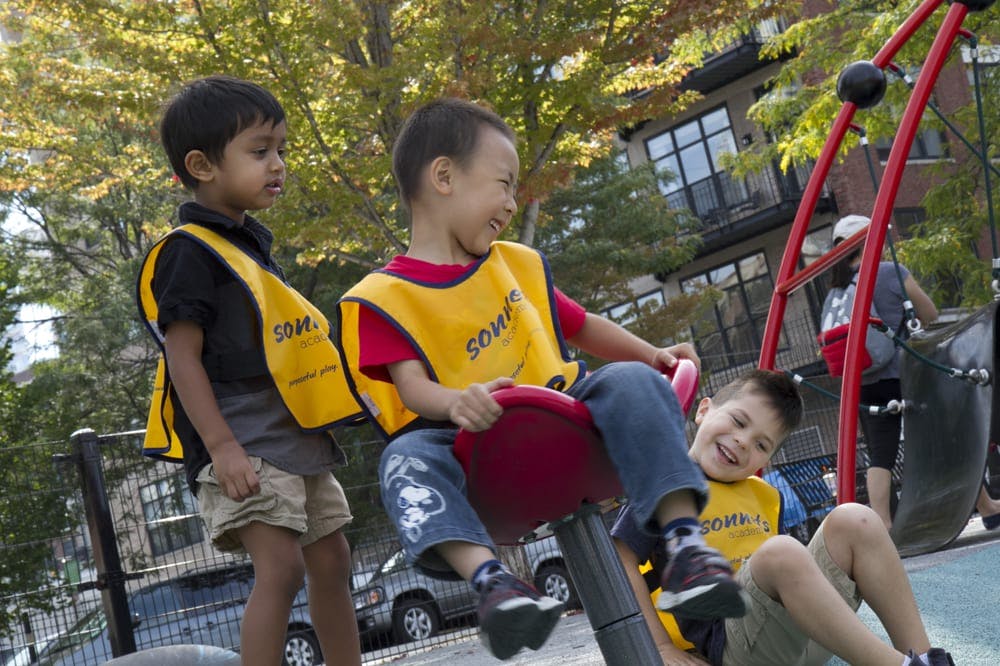 Three children in yellow vests playing on playground equipment