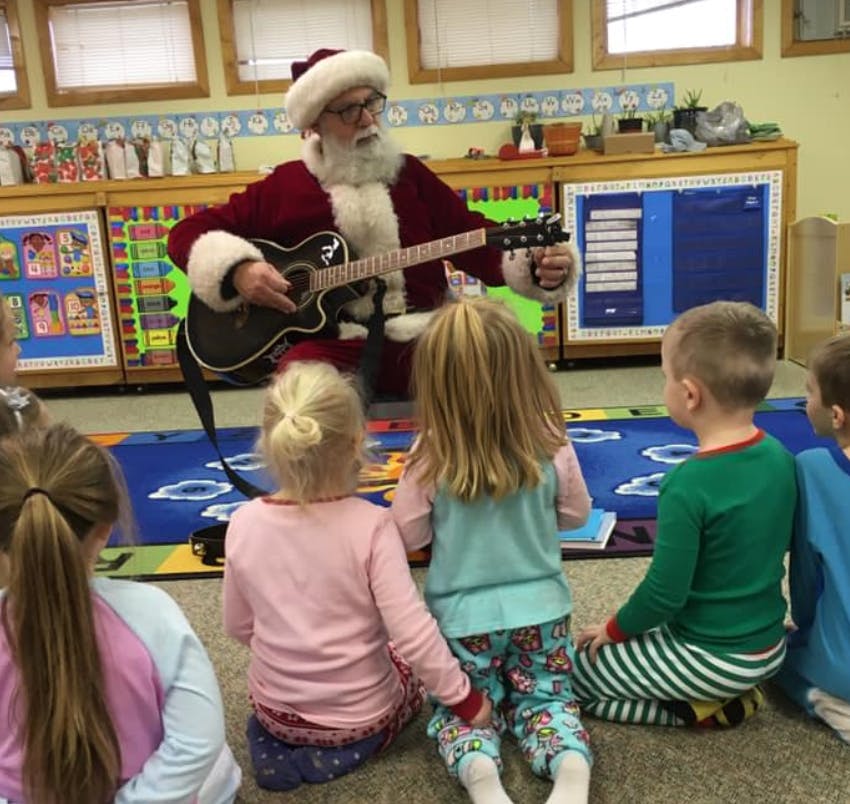 Person dressed as Santa playing guitar for children in a classroom