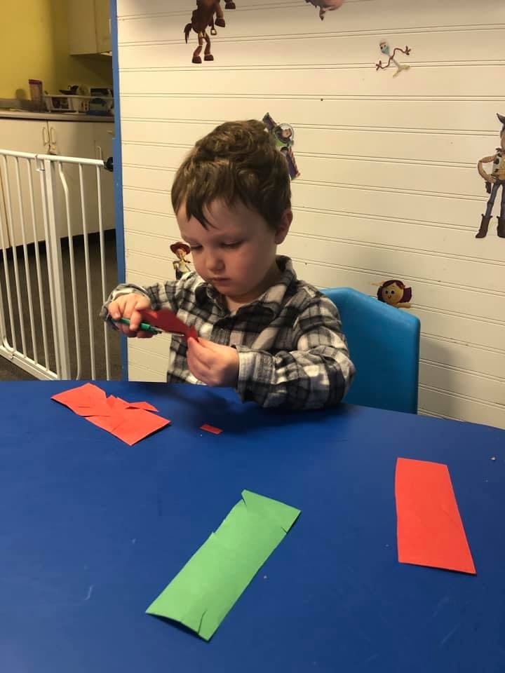 Child cutting red paper with scissors at a table
