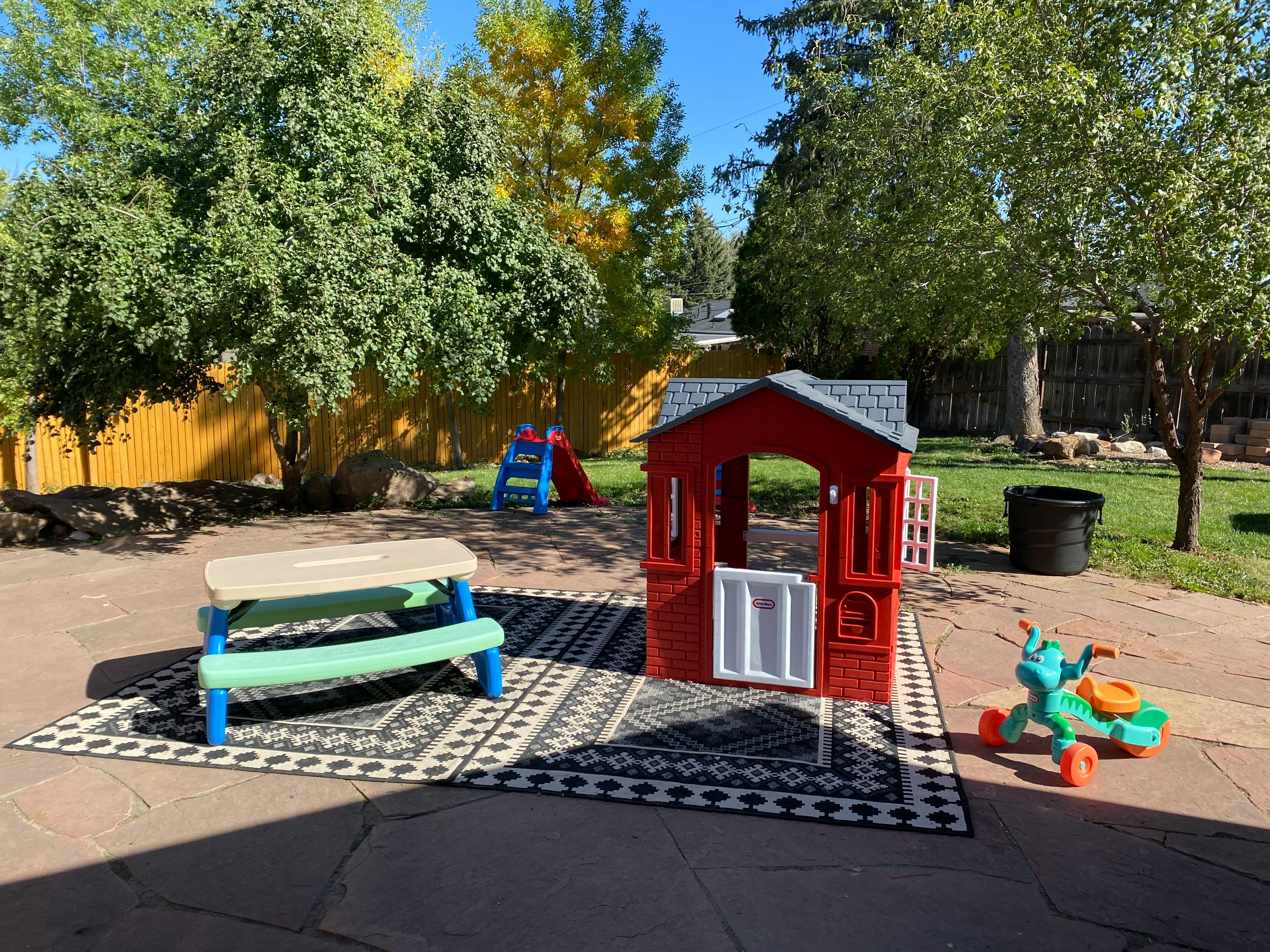 Outdoor play area with a red playhouse, picnic table, and slide