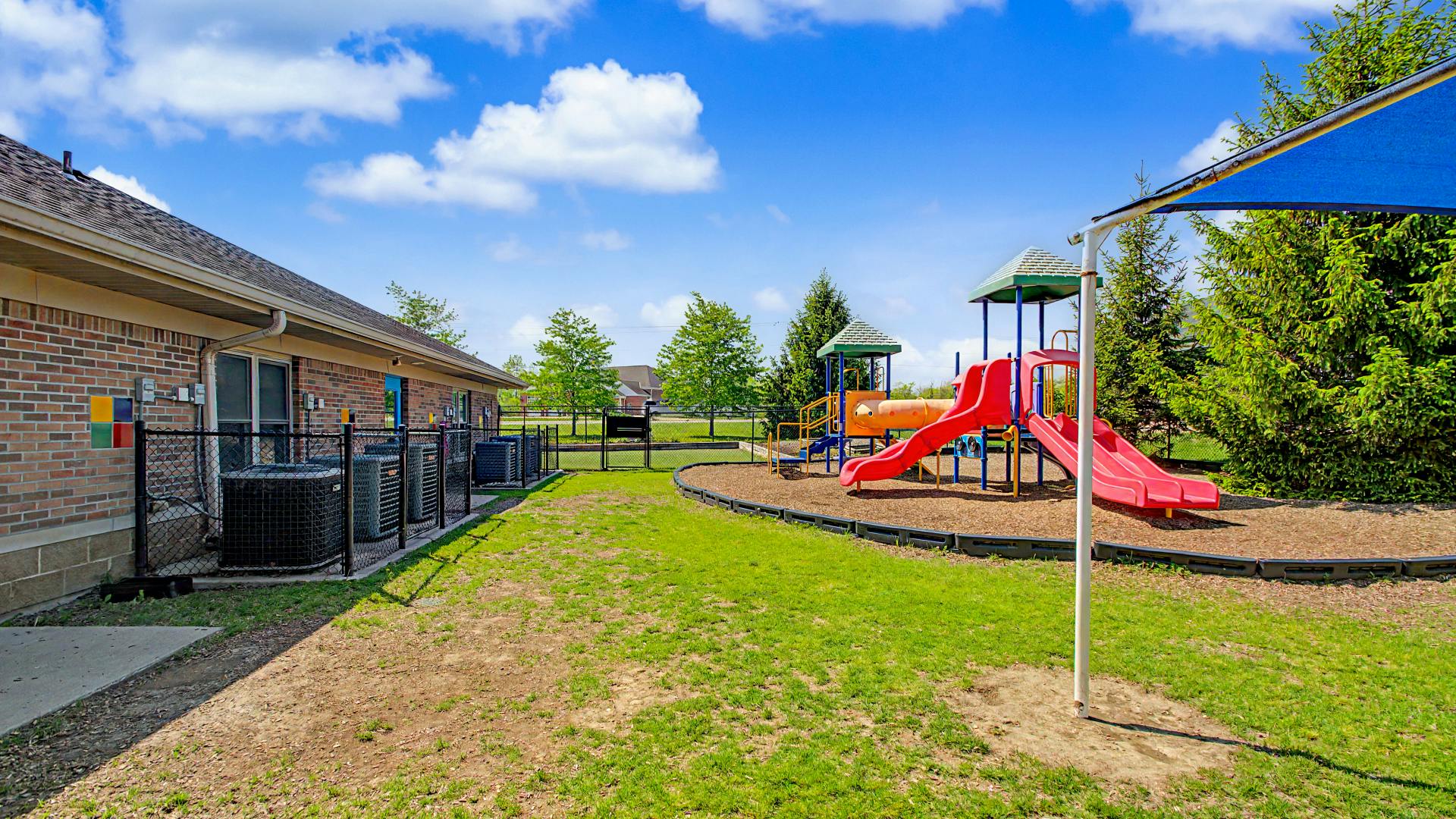 Brick building next to fenced playground with slides and swings on a sunny day