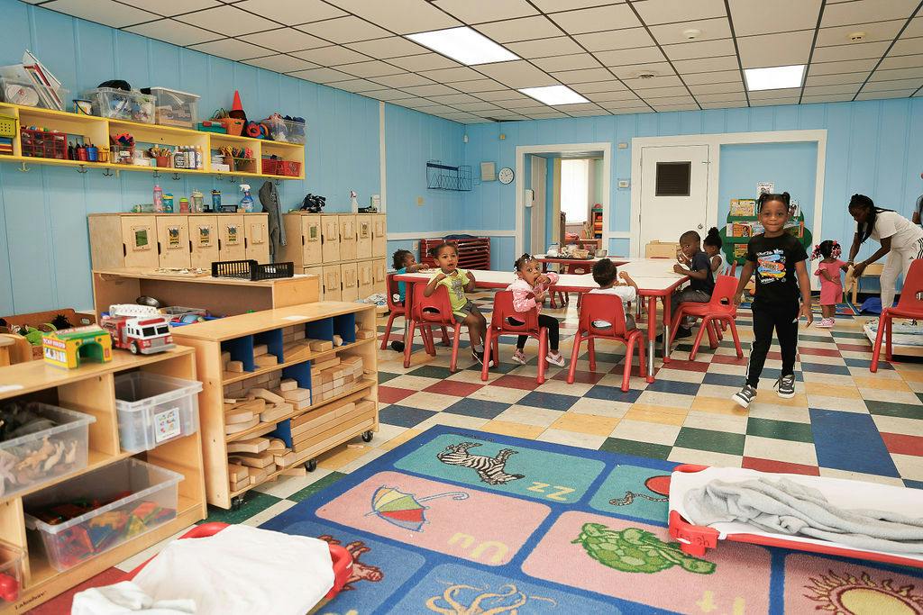 Children in a bright classroom with toy shelves and activity tables