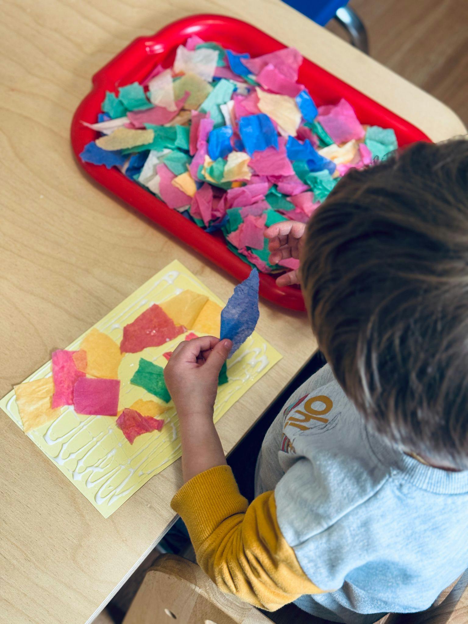 Child doing a craft with colorful paper pieces and glue on a table