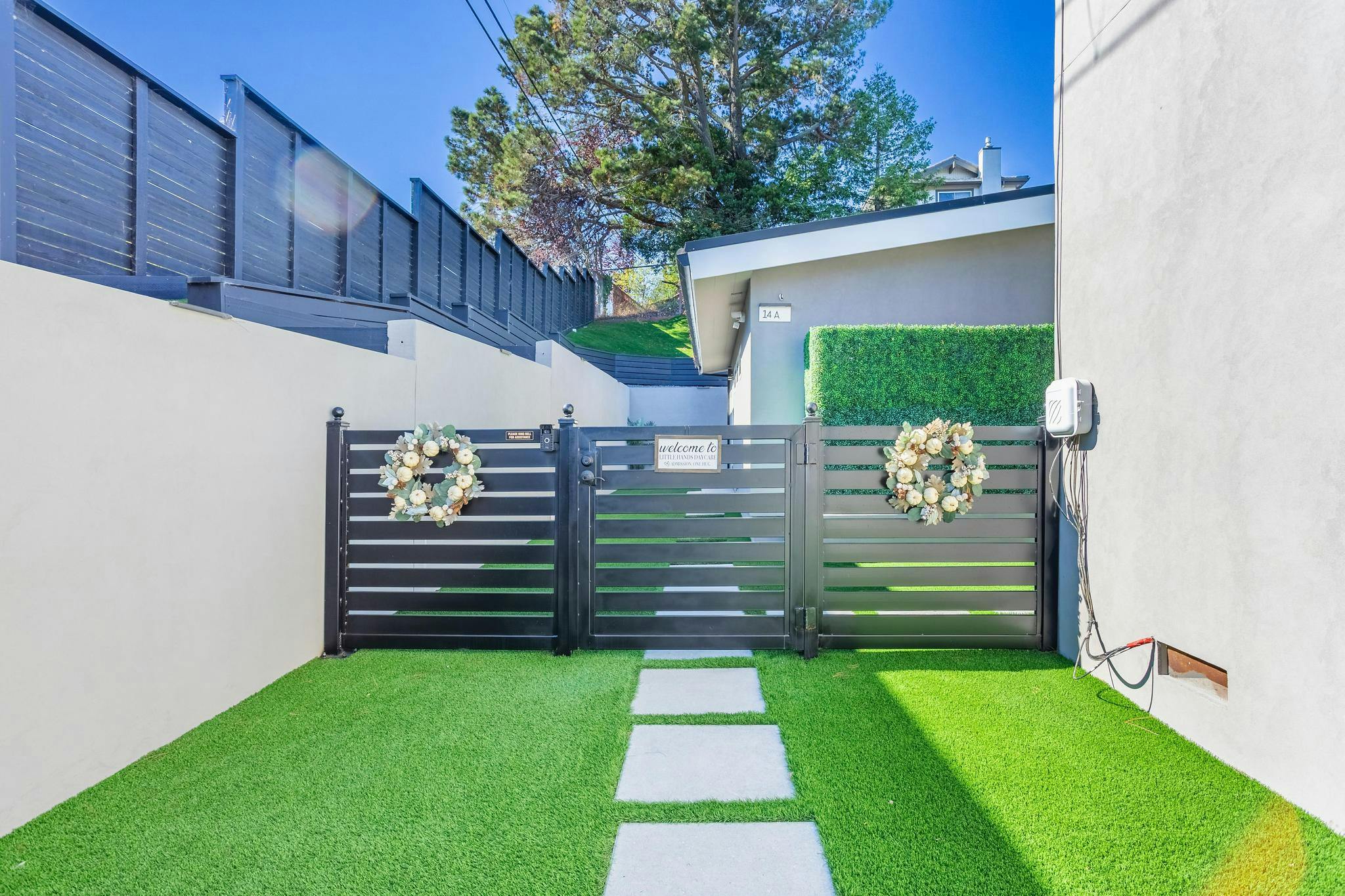Black metal gate with wreaths on a green lawn with stepping stones