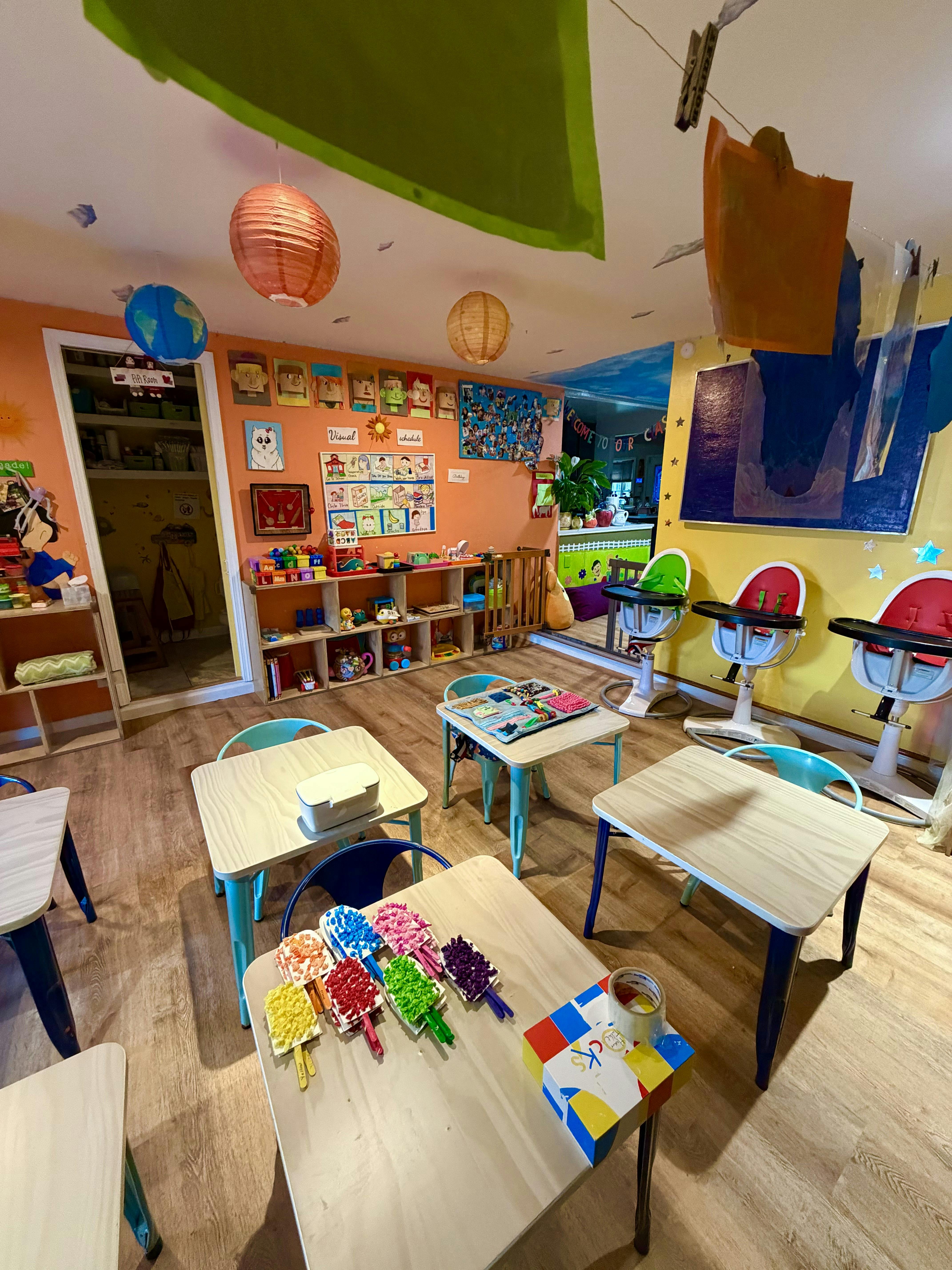 A classroom with small tables and chairs, shelves with toys, and high chairs
