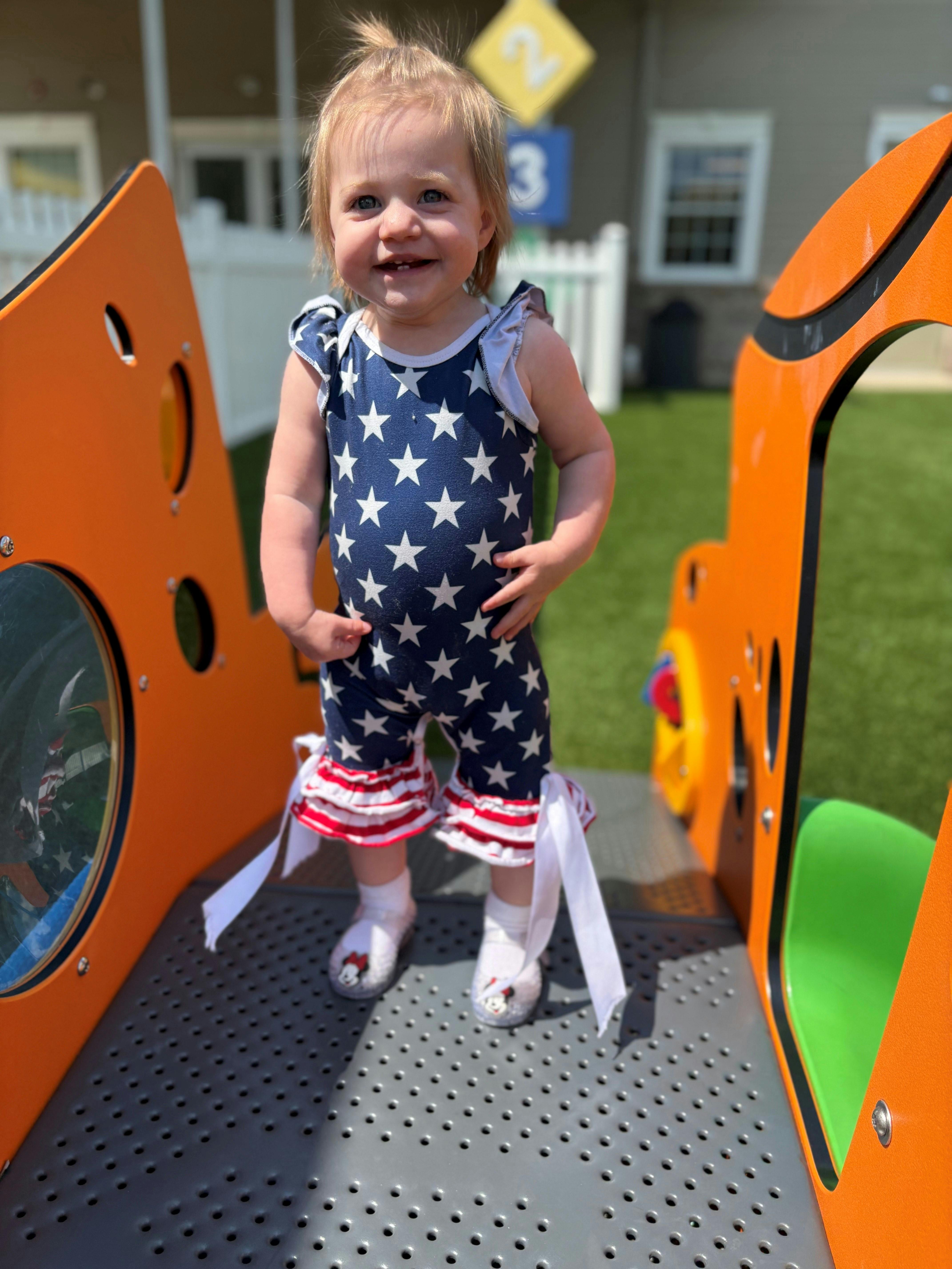 Child in a star-patterned outfit standing on a playground structure
