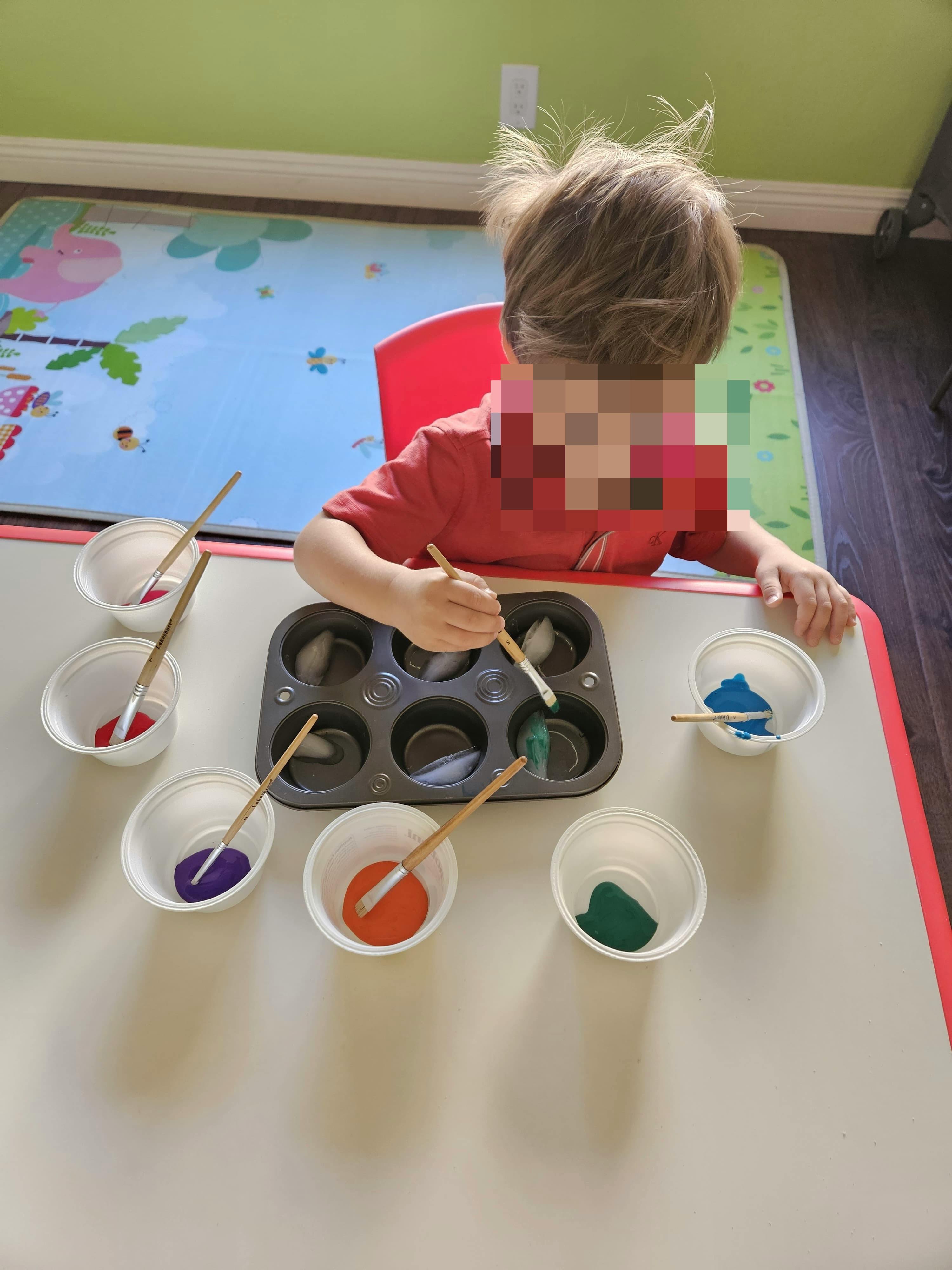 Child painting ice cubes in a muffin tin with various colors of paint