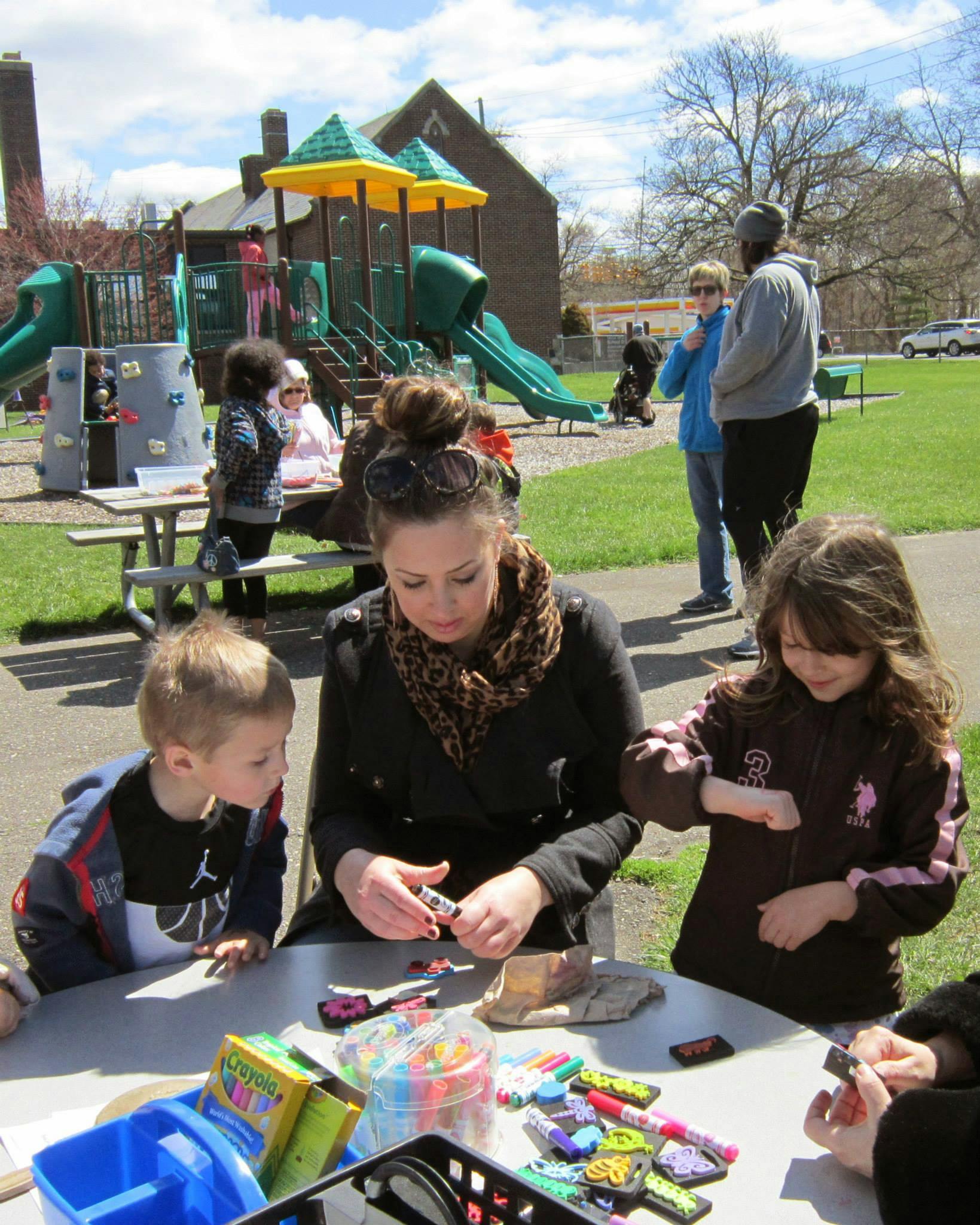 Person and two children at a table with craft supplies in a park