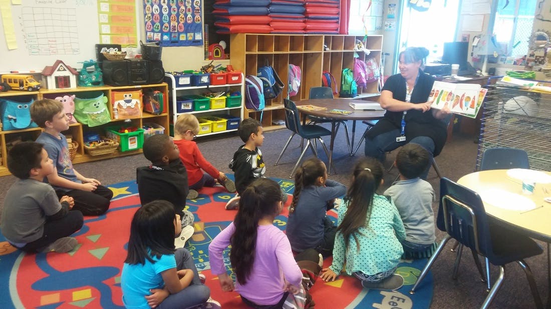 Adult reading a book to children sitting on a rug in a classroom
