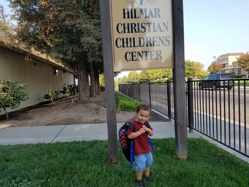 Child with backpack standing next to a sign for Hilmar Christian Childrens Center