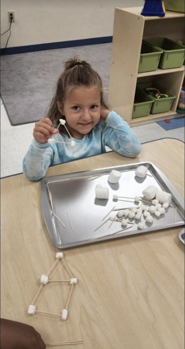 Child holding a marshmallow and toothpick structure