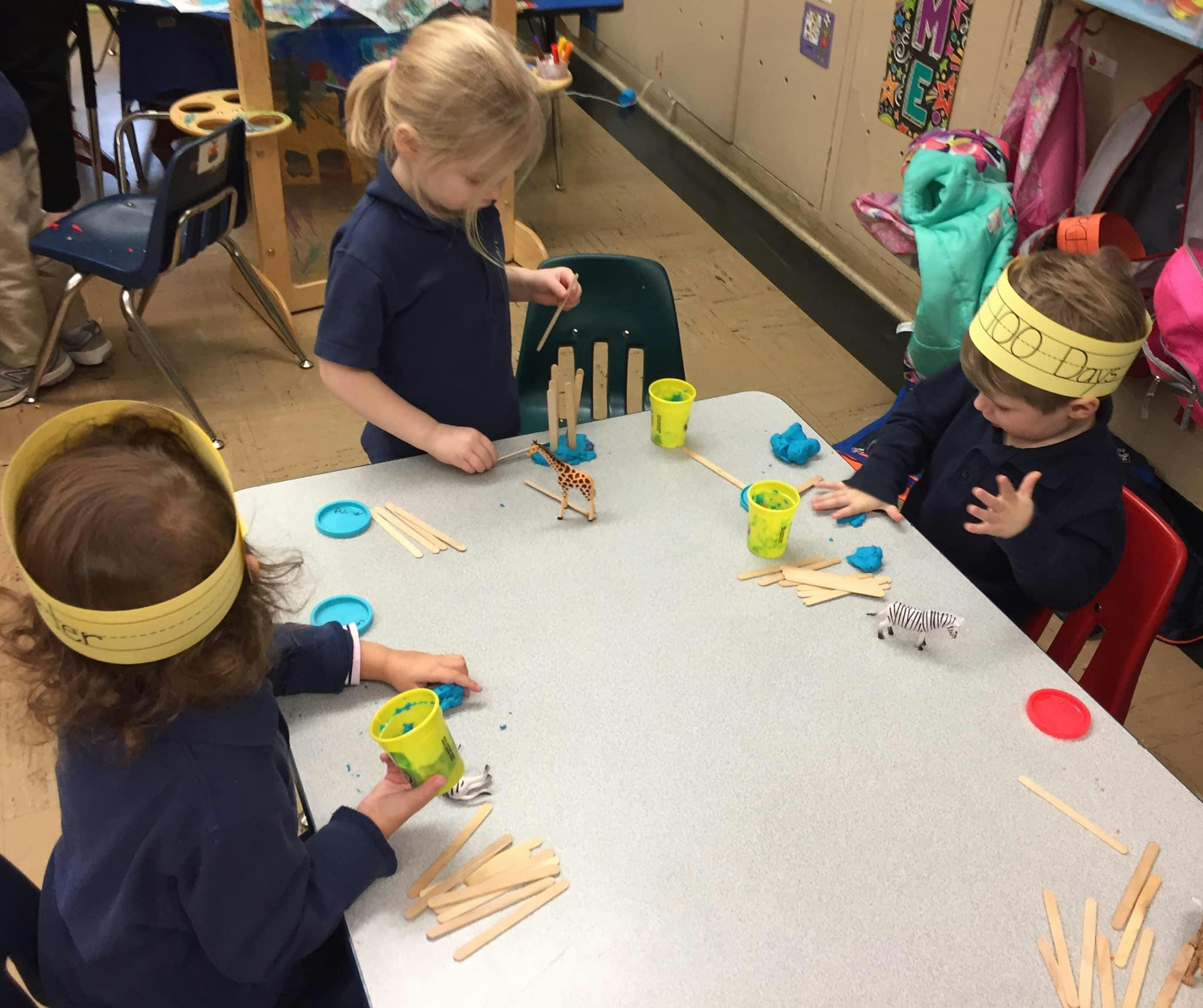 Three children at a table playing with craft sticks and modeling clay
