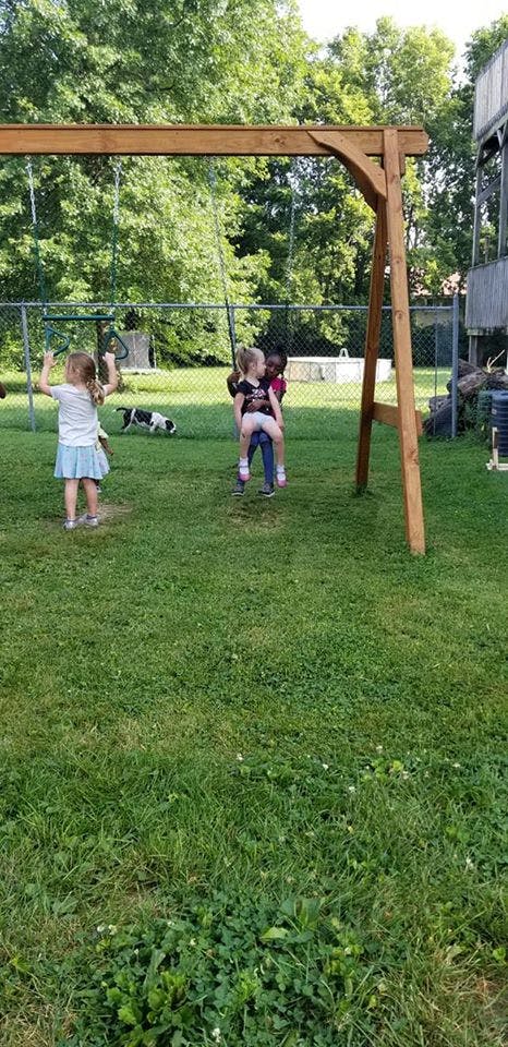 Two children on a swing set, one standing and one sitting on another child's lap