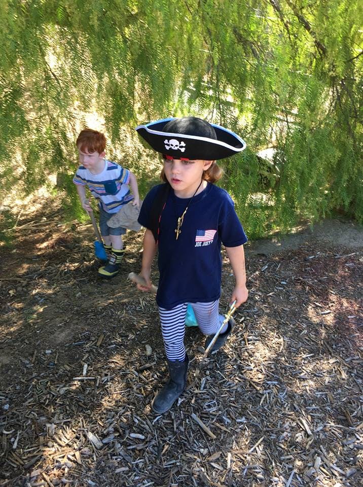 Child in pirate hat and striped pants holding a stick, another child in background