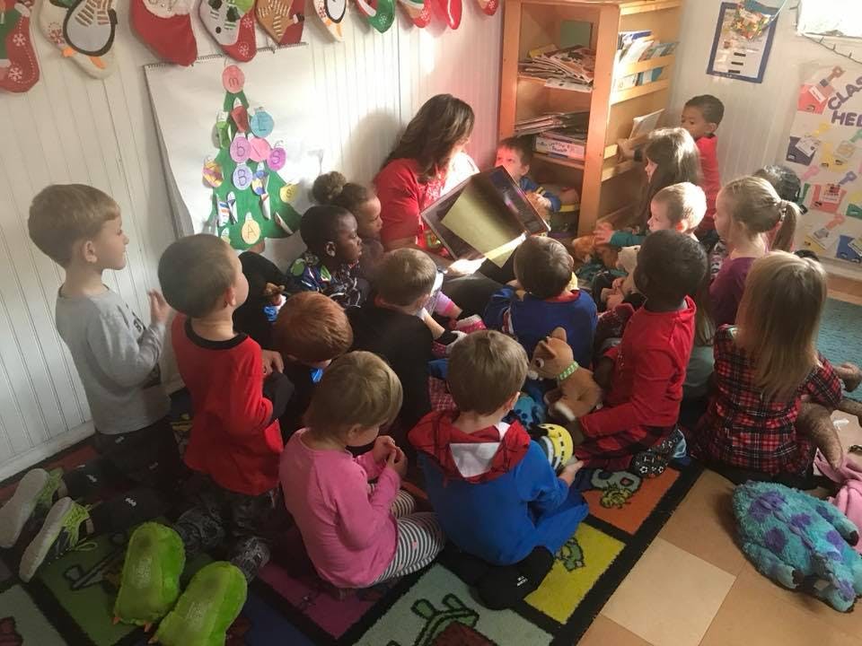 Adult reading a book to a group of children in a classroom