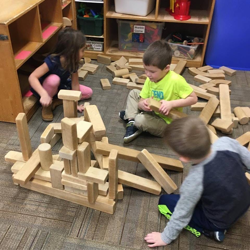 Three children playing with wooden blocks on the floor