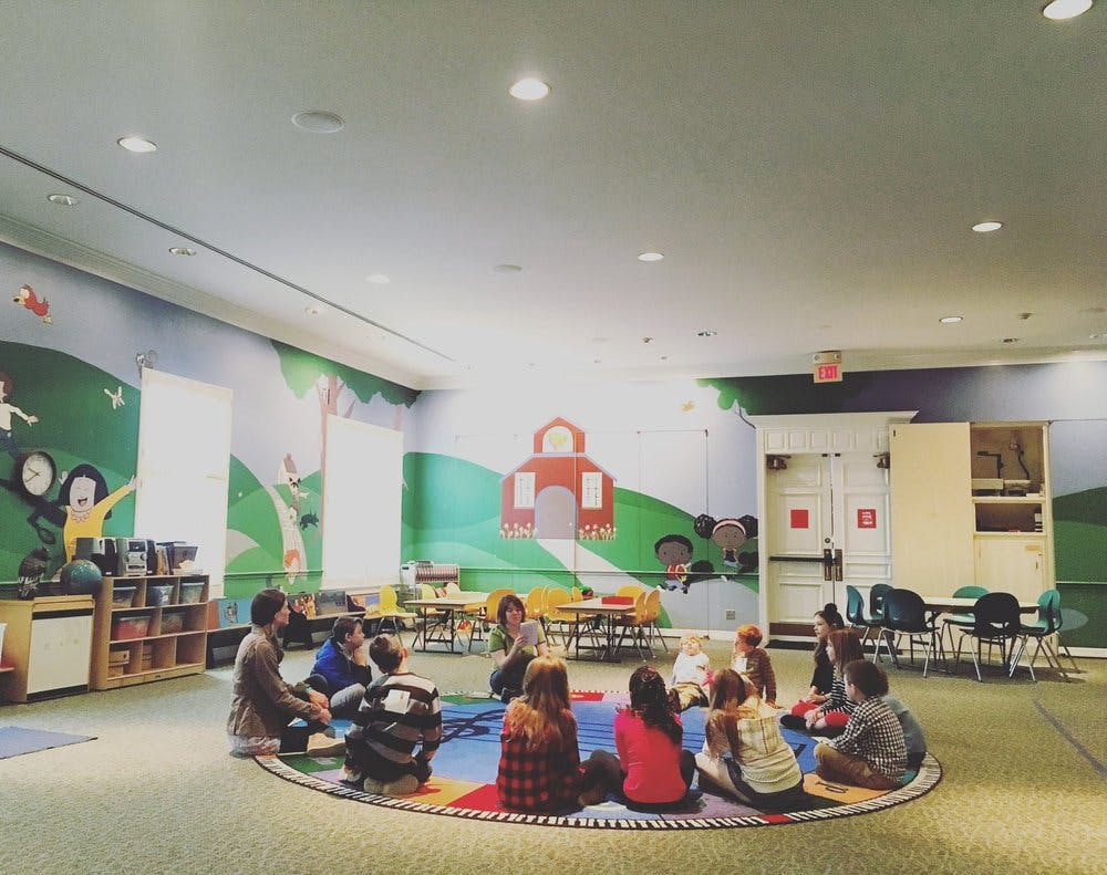 People and children sitting in a circle on a colorful rug in a room with murals