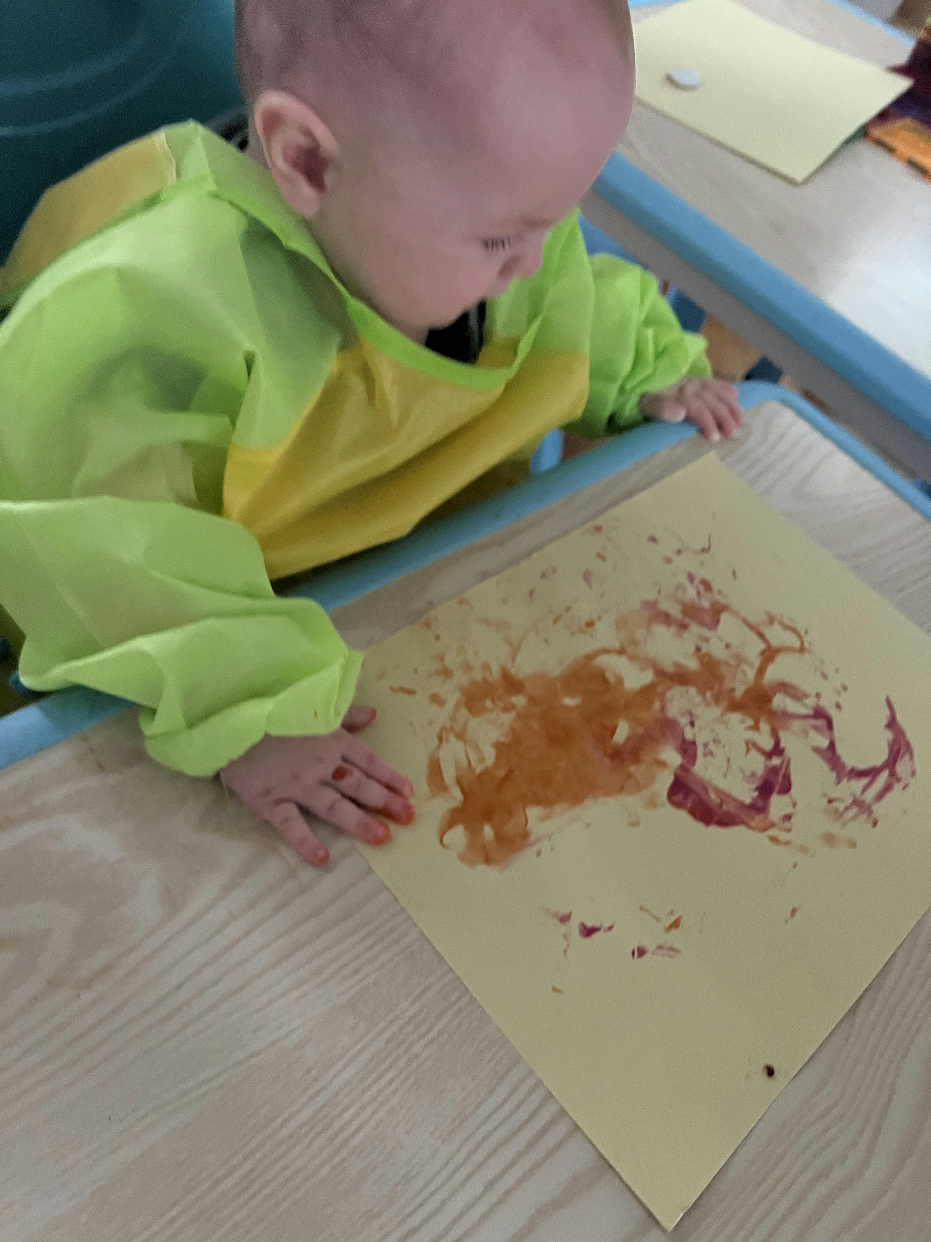 Child wearing an art smock finger painting on paper