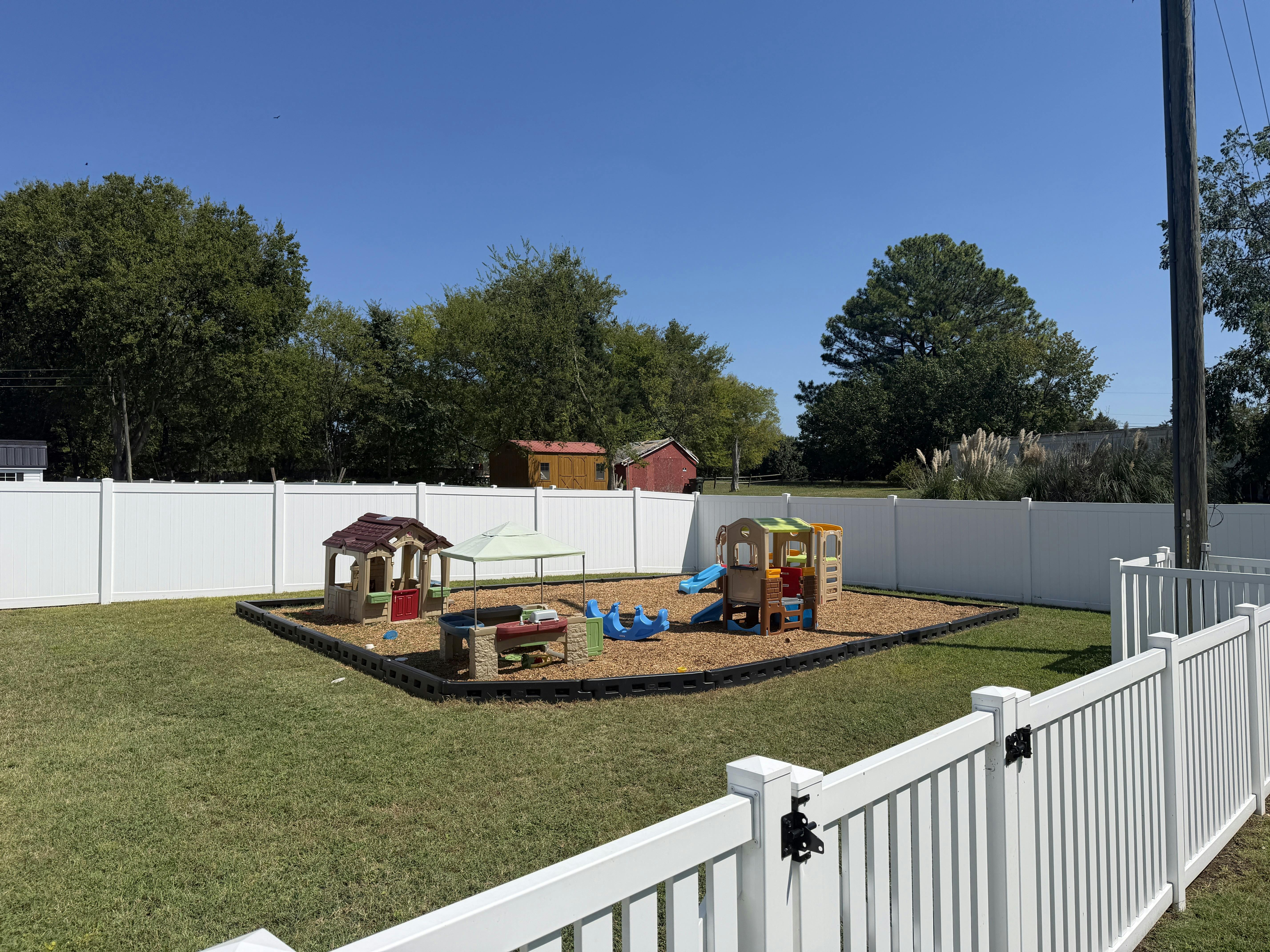 Plastic playground equipment on wood chips inside a fenced backyard