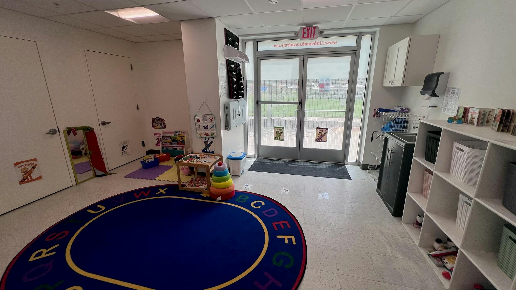 Classroom interior with an alphabet rug and play area near a glass exit door