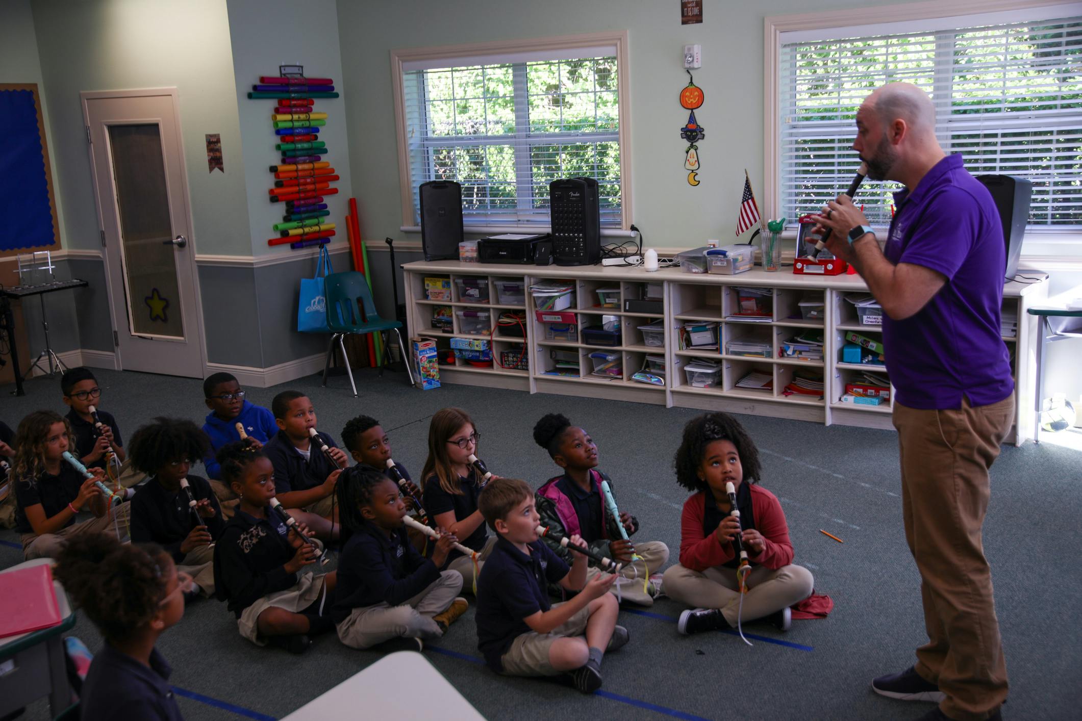 Adult playing a recorder for children sitting on the floor with recorders